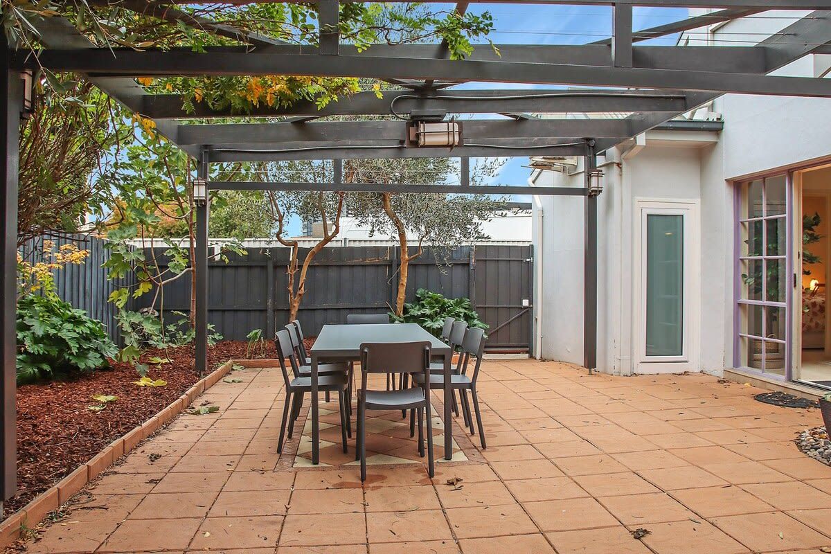 Un patio con una mesa, sillas, una pérgola y vistas a una casa.