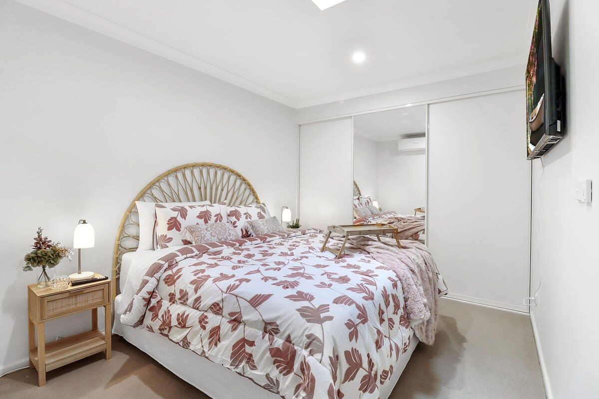 A bedroom with a bed, bedside table, lamp, and a large mirror.