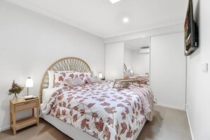 Een slaapkamer met een bed, nachtkastje, lamp en spiegel.