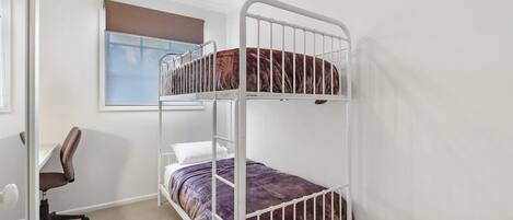 A bunk bed with a desk and chair, a window with blinds, and a door.