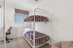 Een stapelbed met bureau en stoel, een raam met zonwering, en een lichtgekleurde vloer.
