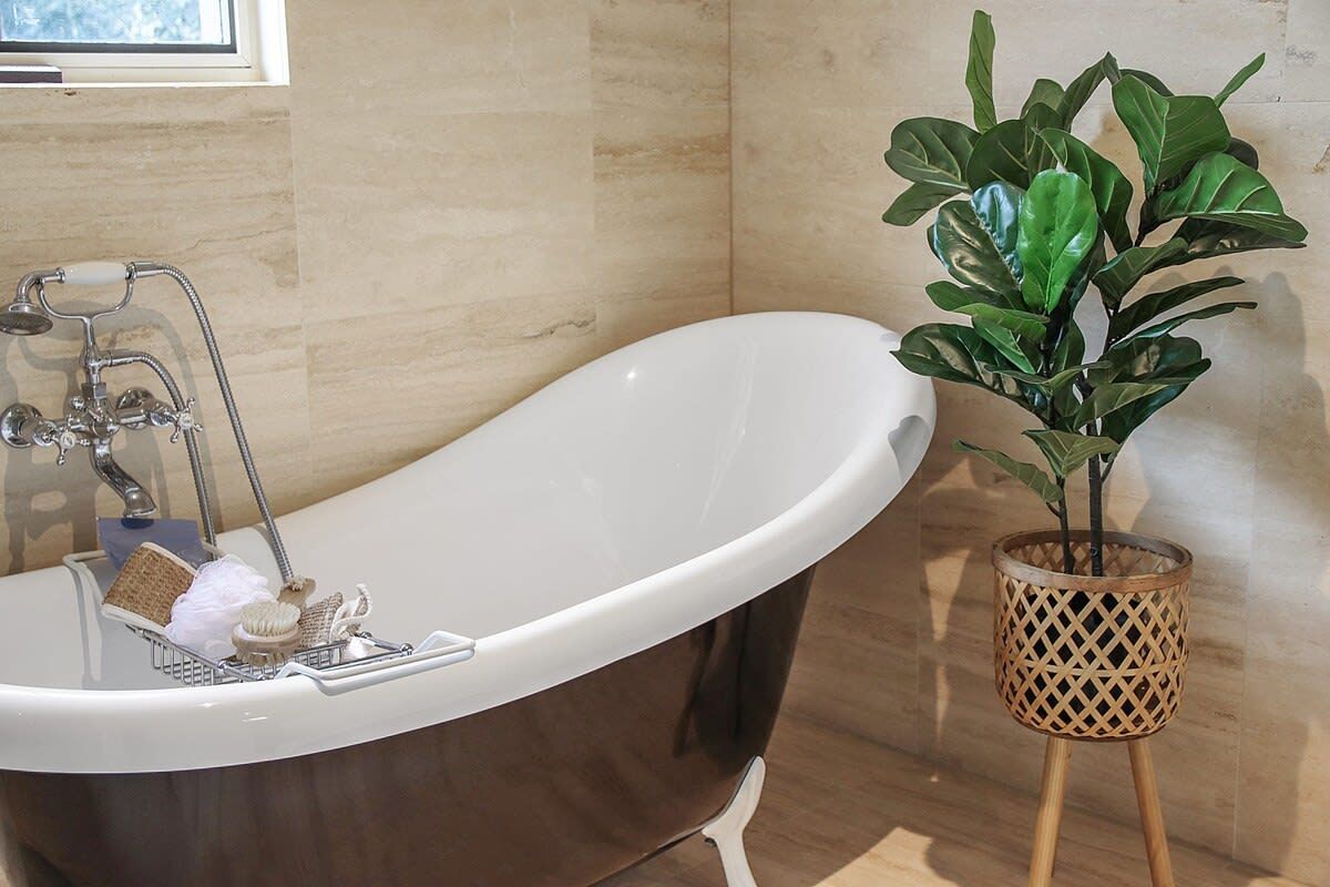 Une salle de bain avec une baignoire sur pieds, un support à plantes en bois et une fenêtre située au-dessus de la baignoire.