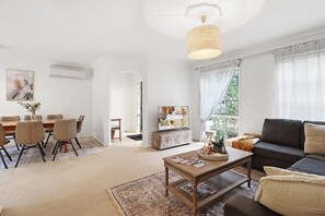 A living room with a sofa, coffee table, and TV. There's a dining area with chairs and a table.