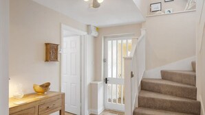 A hallway with a wooden console table, a white door, and a staircase with beige carpet. - Idyllic Cottage in Heart of Devon Countryside (Cullompton)
