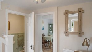 A hallway with a wooden door, a radiator, a table with a lamp, and a mirror on the wall. - Idyllic Cottage in Heart of Devon Countryside (Cullompton)