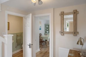 A hallway with a wooden door, a radiator, a table with a lamp, and a mirror on the wall. - Idyllic Cottage in Heart of Devon Countryside (Cullompton)