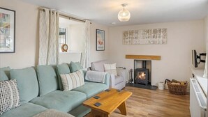 A cozy living room with a sofa, a wooden coffee table, a fireplace, and a hanging light fixture. - Idyllic Cottage in Heart of Devon Countryside (Cullompton)