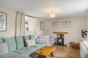 Een gezellige woonkamer met een bank, een houten salontafel, een open haard en een hanglamp.