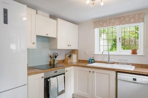 A modern kitchen with white cabinets, a Bosch dishwasher, a built-in oven, and a window with a view of greenery.