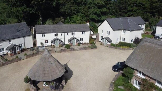 A residential area with white houses, a thatched-roof structure, and a car parked nearby. - Idyllic Cottage in Heart of Devon Countryside (Cullompton)