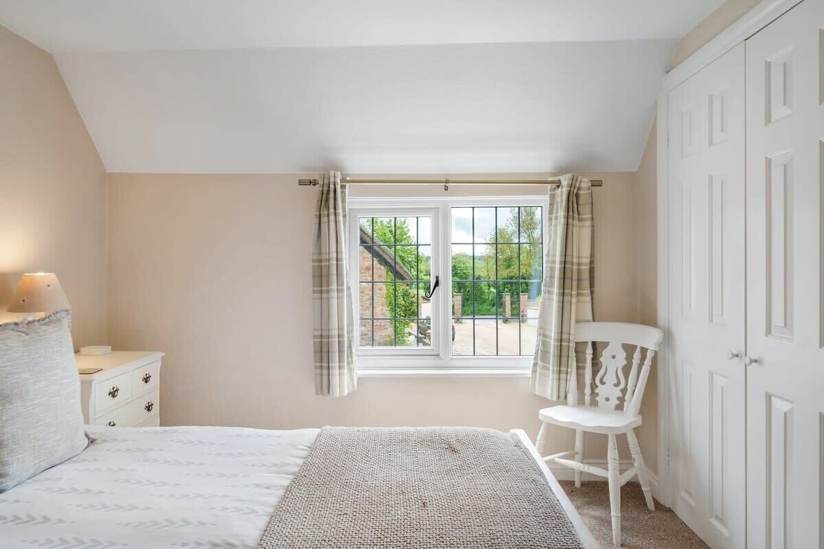 A bedroom with a bed, a nightstand, a chair, a wardrobe, and a window with curtains.