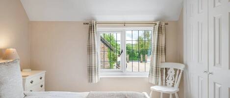 A bedroom with a bed, a nightstand, a chair, a wardrobe, and a window with curtains.
