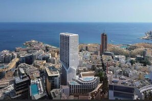 Un immeuble de grande hauteur au design moderne, entouré d’autres constructions urbaines et bordé par une côte.