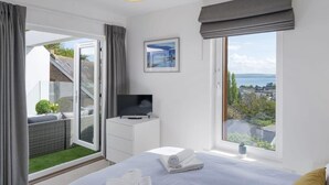 Une chambre d’hôtel moderne dotée d’un lit, d’une télévision, d’une vue sur la ville et d’un balcon aménagé avec du mobilier d’extérieur.