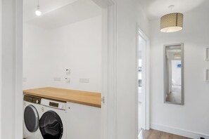 A laundry room with a washing machine and dryer, a wooden countertop, and a hanging light fixture. - Apartment with Stunning Sea Views, Private Parking (Torquay)