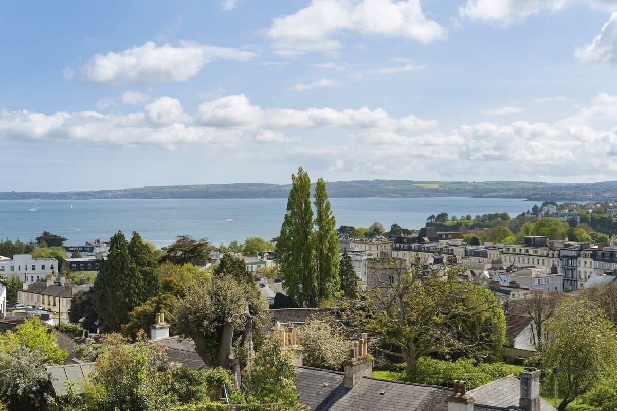 A coastal town with buildings and trees, a clear sky, and a view of the sea.