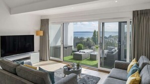 Un salon moderne doté d’un téléviseur à écran plat, de canapés gris, d’une table basse et d’un balcon offrant une vue sur la mer.