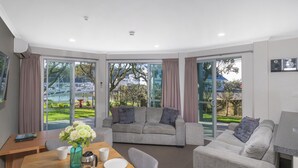 A modern living room with a dining area, grey sofas, a coffee table, and a view of a marina through large glass doors.