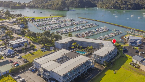 A marina with numerous boats, a parking area, and buildings with a swimming pool.