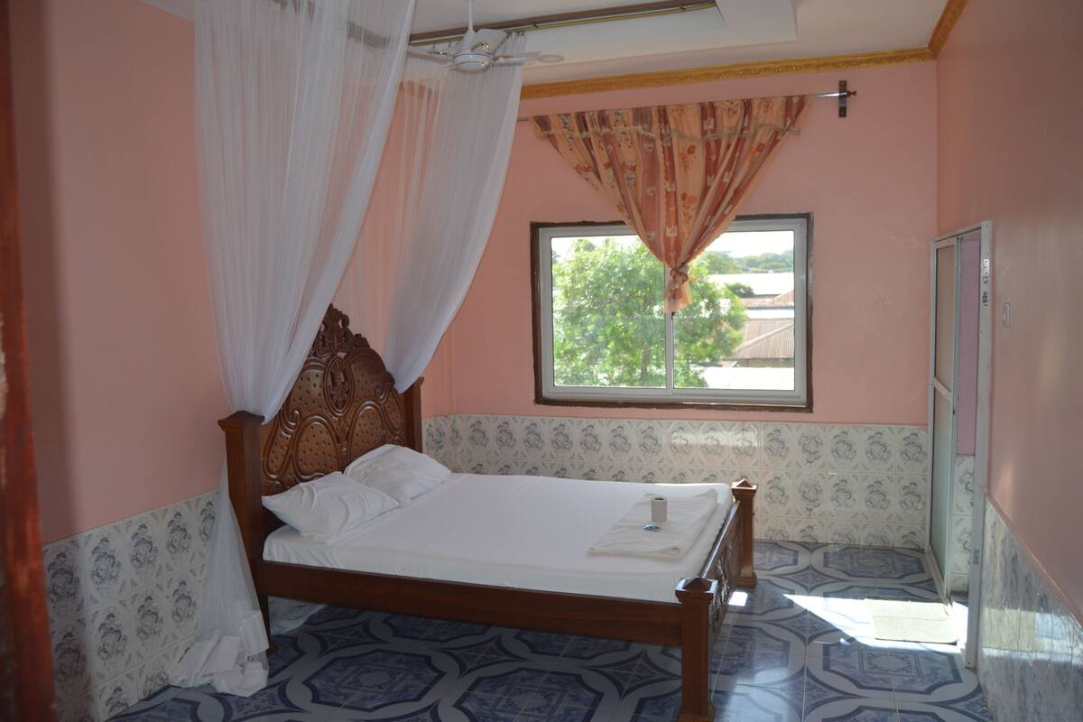 Un dormitorio con cama, ventana con cortinas, una puerta y baldosas de suelo estampadas.