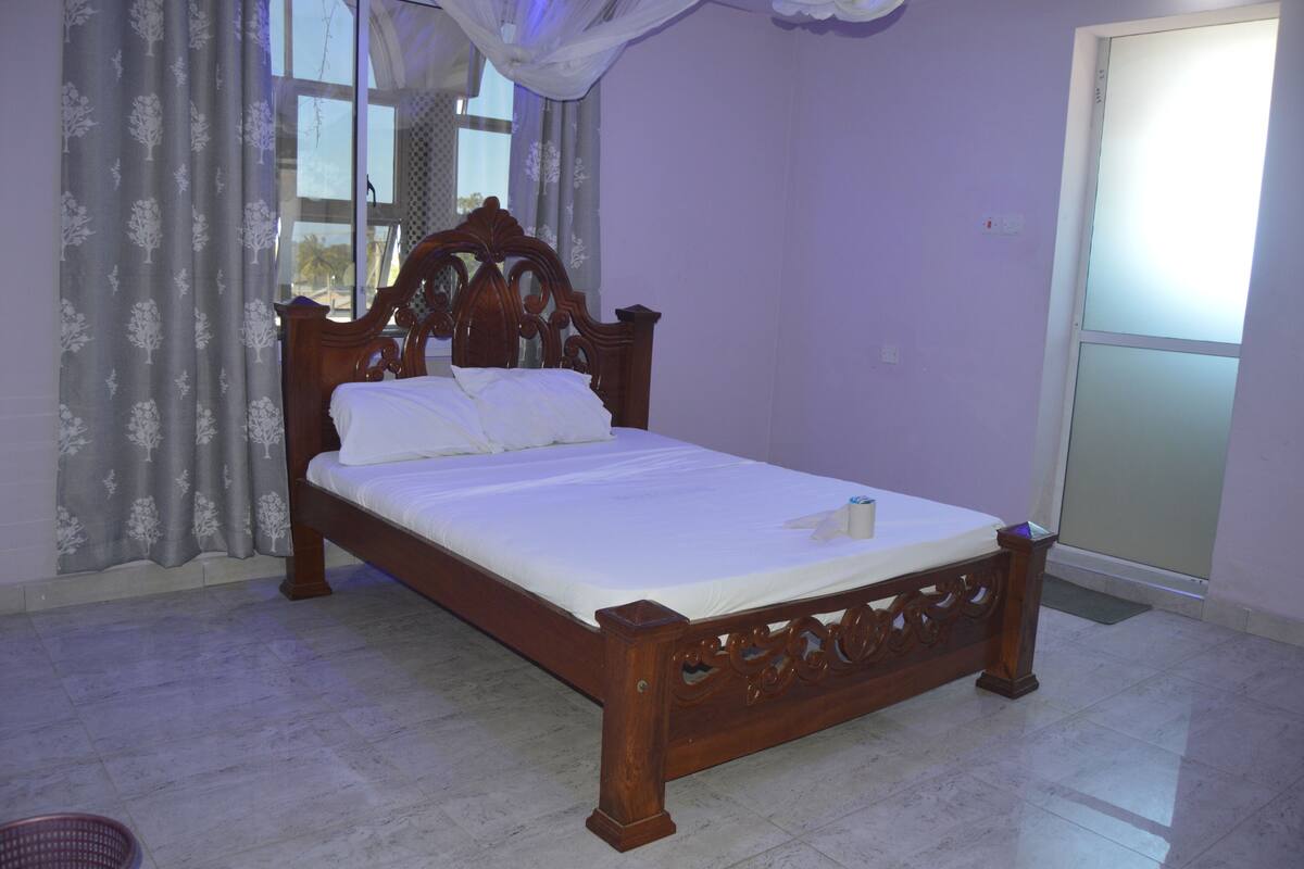 Una cama bien hecha en una habitación con un ventanal, cortinas y una puerta.