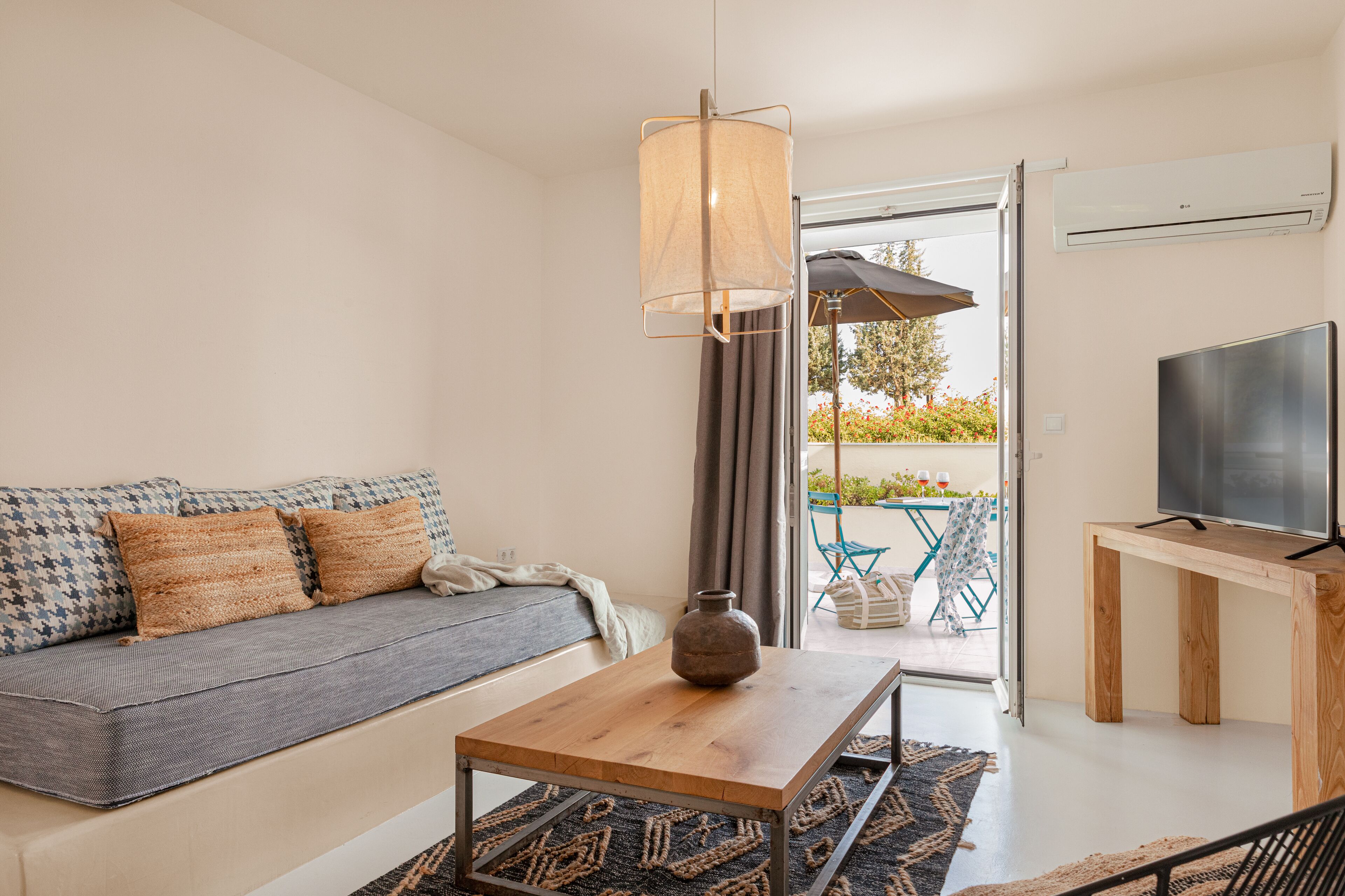 Una sala de estar moderna con un sofá, una mesa de centro de madera, un televisor sobre un mueble bajo y vistas al patio exterior.