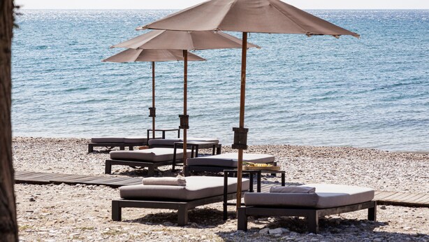 En strand med solstolar och parasoller, ett trädäck och utsikt över havet.