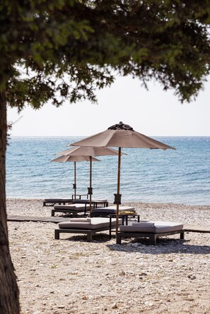 Een strand met ligbedden en parasols, een houten terras en uitzicht op de zee.