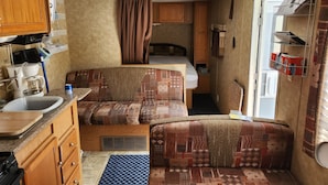 A compact RV interior with a kitchenette, a bed, and a small seating area.