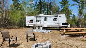A recreational vehicle with a picnic table and chairs in a wooded area.
