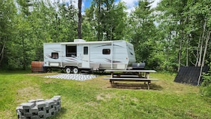 A recreational vehicle (RV) parked in a grassy area with a picnic table and a grill nearby.