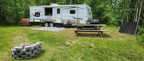 Una caravana estacionada en una zona verda amb una taula de picnic i una barbacoa a prop.