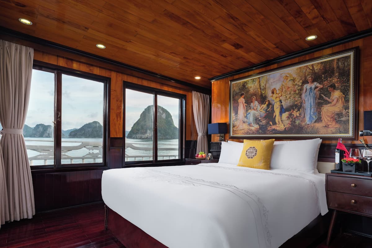 A large bed with a white bedspread, a yellow pillow, and a painting above it.