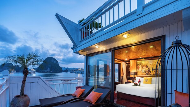Een balkon met ligbedden en een bloempot, een slaapkamer met een bed en een schilderij, en een uitzicht op boten op het water.