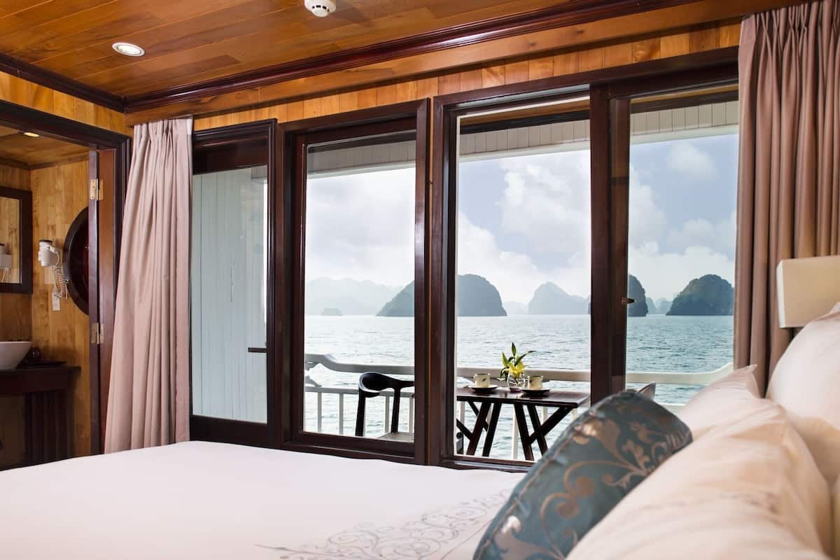 A bedroom with a large window overlooking the sea, a bed, a small table with a chair, and wooden paneling.