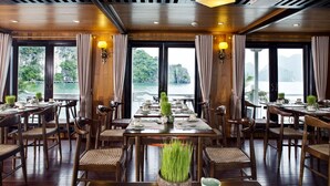 Een restaurant met houten meubels, grote ramen met gordijnen en uitzicht op water en groen.