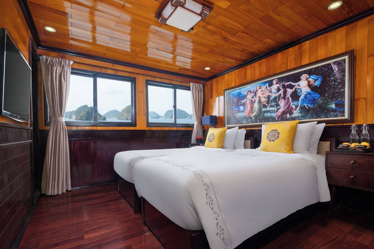 A hotel room with a large bed, wooden flooring, a painting on the wall, and a view of the sea through the windows.