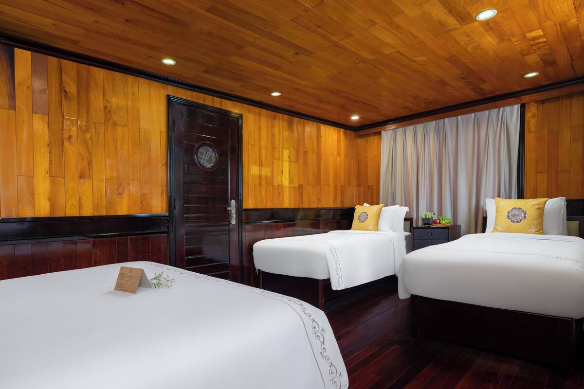 A hotel room with two beds, wooden paneling on the walls, a dark wooden door, and a window with curtains.