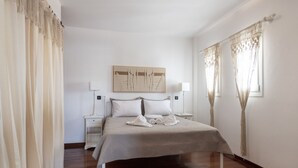 A bedroom with a bed, two bedside tables, a wall-mounted artwork, and a window with curtains. - Vagia Calm House 2 (Paros)