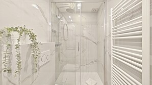 Een moderne badkamer met een douche met glazen wand, marmeren wanden en een witte handdoekhouder.