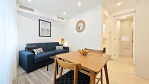 Een moderne woonkamer met een blauwe bank, een houten eettafel en een vloerkleed met een patroon.