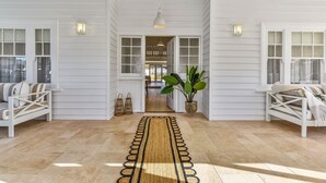 A hallway with white walls, a wooden floor, and a central rug leading to a room.