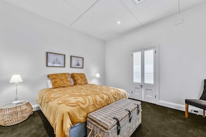 A bedroom with a bed, two pillows, a bench, a lamp, a wicker chair, and two framed pictures on the wall. - Hawdon House (Robe)