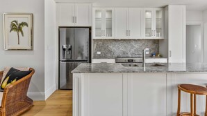 A modern kitchen with white cabinetry, a granite countertop, and a stainless steel refrigerator.