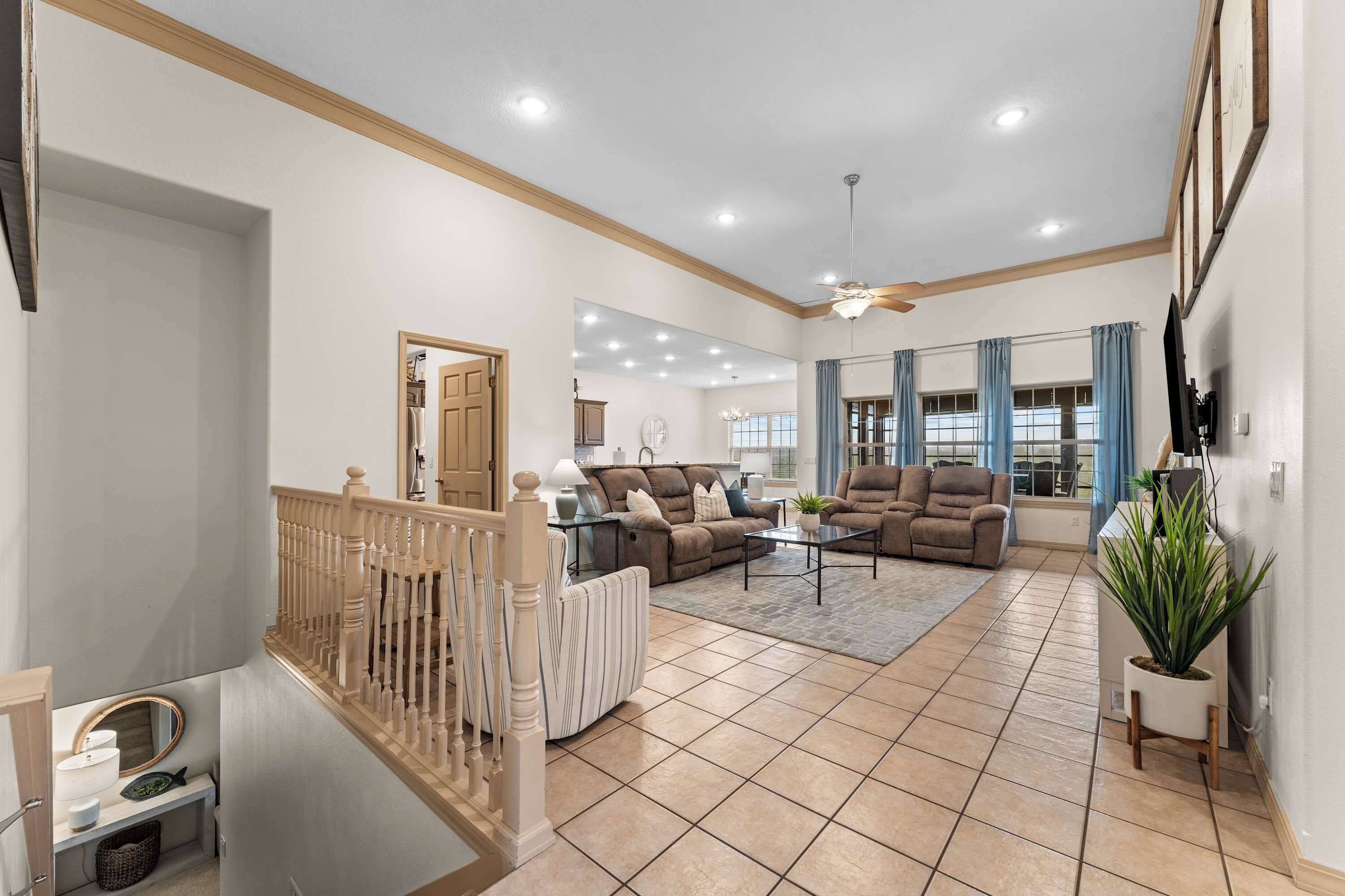 A spacious living room with a high ceiling, a staircase, and a view of the kitchen.