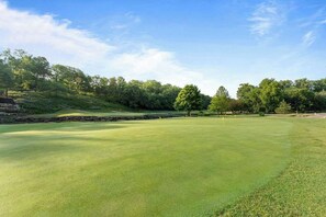 Ein Golfplatz mit gepflegtem Grün, Bäumen und blauem Himmel.