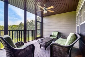 A covered porch with wicker furniture, a ceiling fan, and large windows offering a view of greenery.