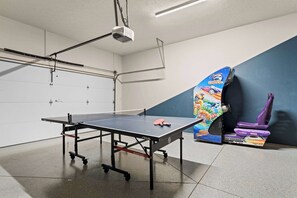 A ping pong table with a net, a projector, and a wall-mounted rack.