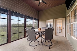 A covered patio with a table and chairs, large windows, and a ceiling fan.