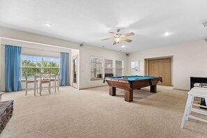 A spacious room with a pool table, a ceiling fan, and a door leading to an outdoor area.